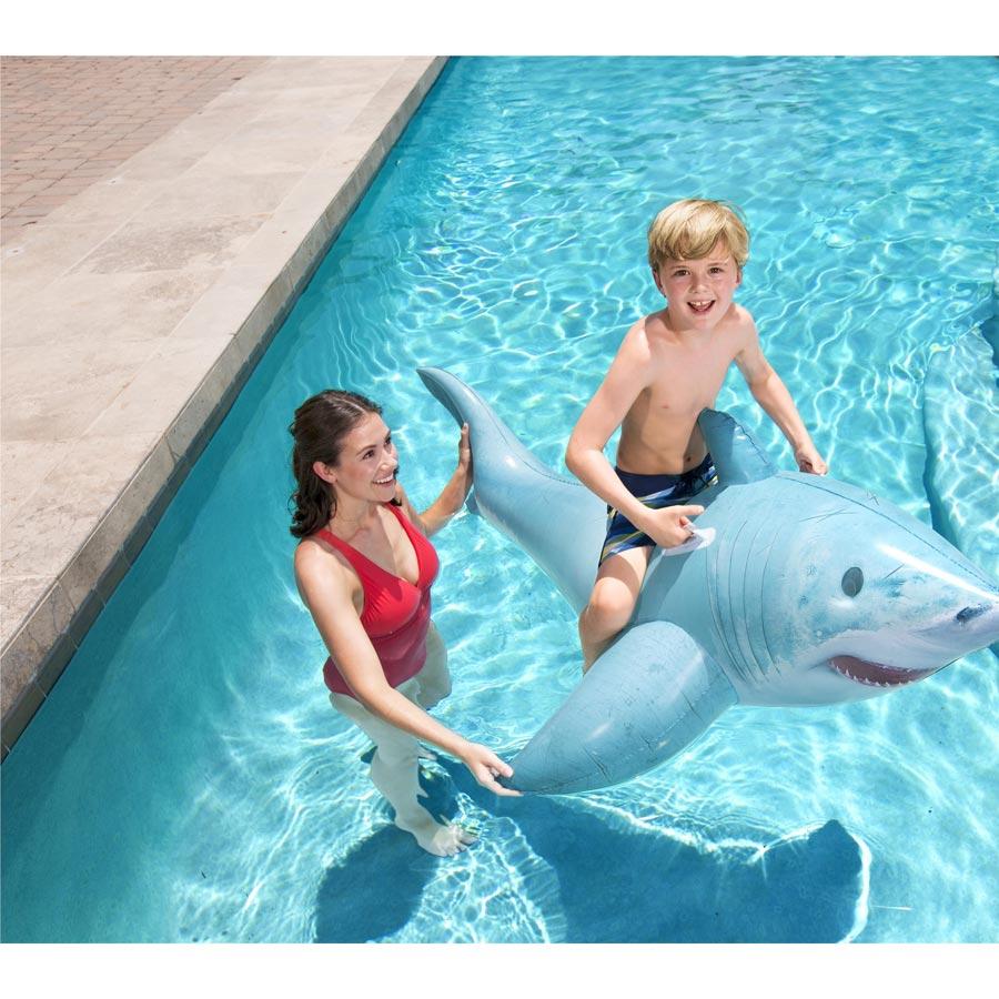 A child and adult playing with a shark-shaped inflatable pool toy in a pool.