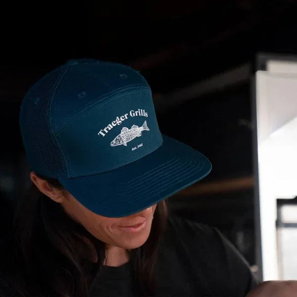 Person wearing a blue cap with 'Traeger Grills' logo on a dark background